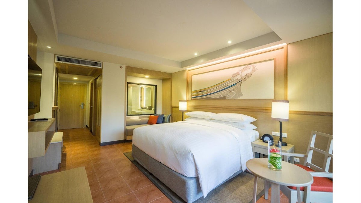 Resort guest room with queen bed, wooden headboard, illuminated boat artwork, side tables with lamps, and terracotta tile flooring.