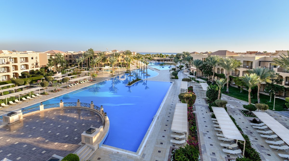 Aerial view of Jaz Aquamarine Resort showing multiple bright blue pools, palm trees, sun loungers, and beige resort buildings along the Red Sea coast.
