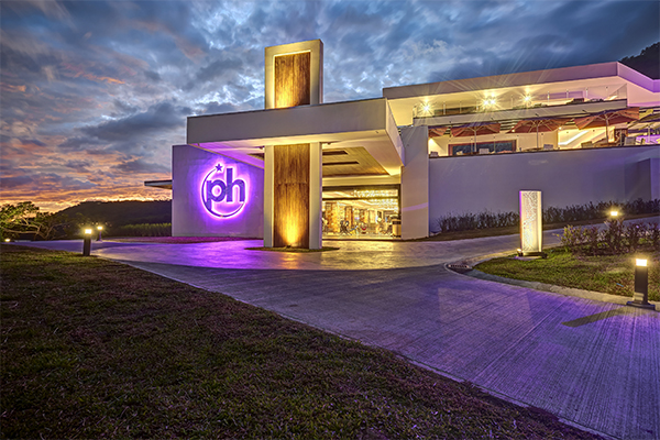 Planet Hollywood Costa Rica's modern entrance glows with purple neon signage at dusk under a dramatic cloudy sky.