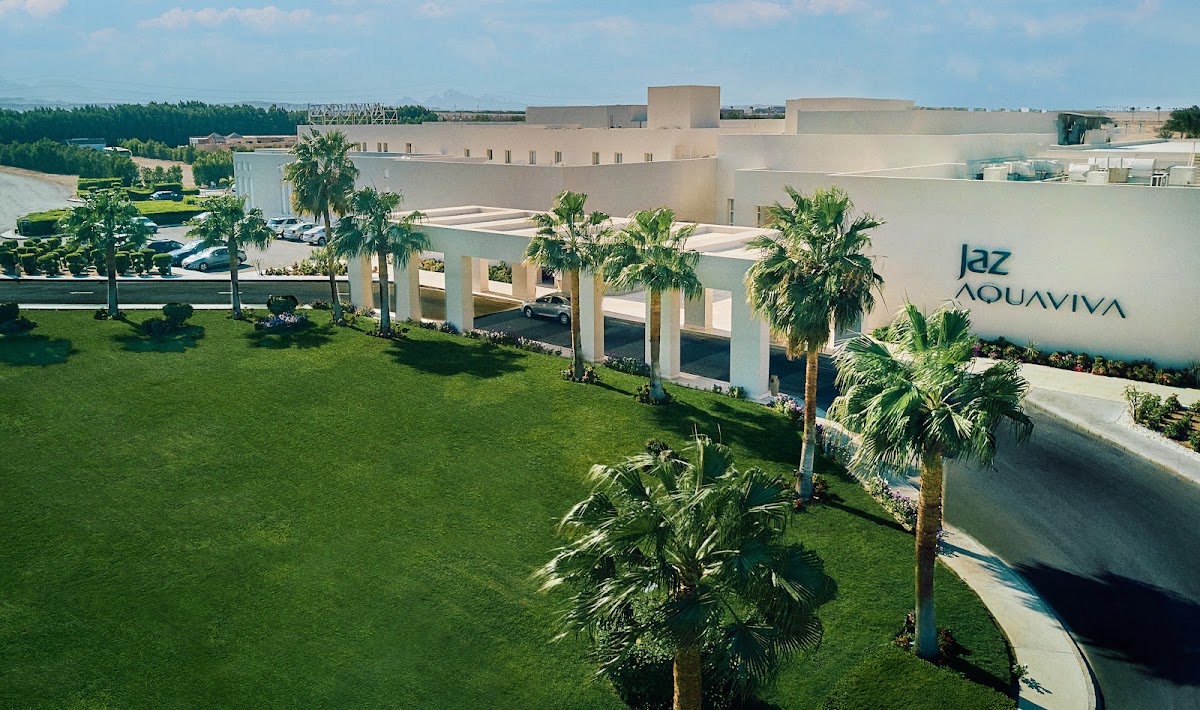JAZ Aquaviva's modern beige buildings with palm trees and manicured lawns under blue sky.
