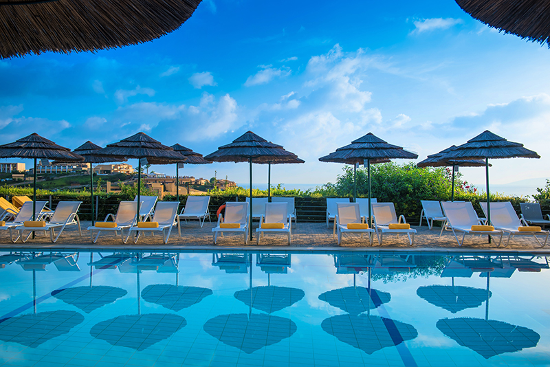 Pool with lounge chairs and thatched umbrellas under blue sky at Blue Bay Resort Hotel.