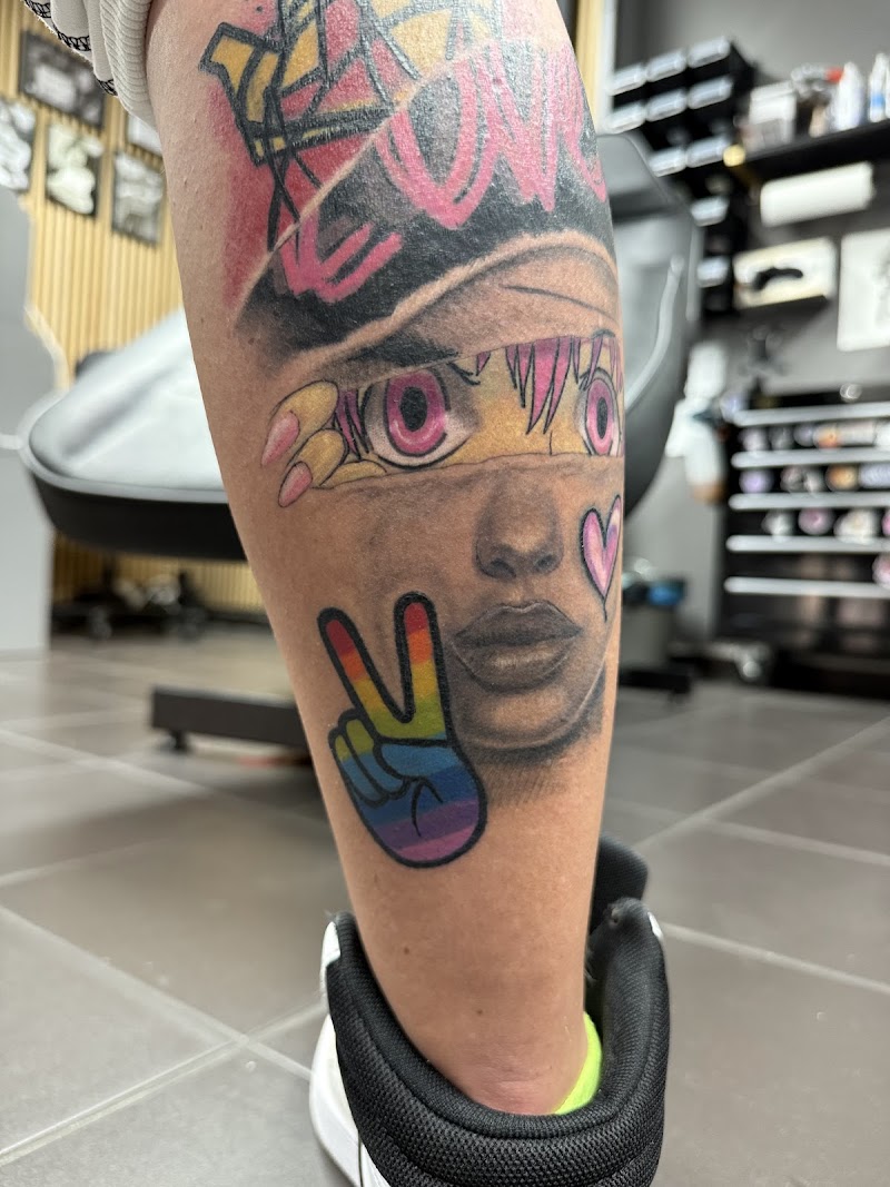 Kleurrijke tattoo op onderbeen met portret, regenboog vredesteken en graffiti.