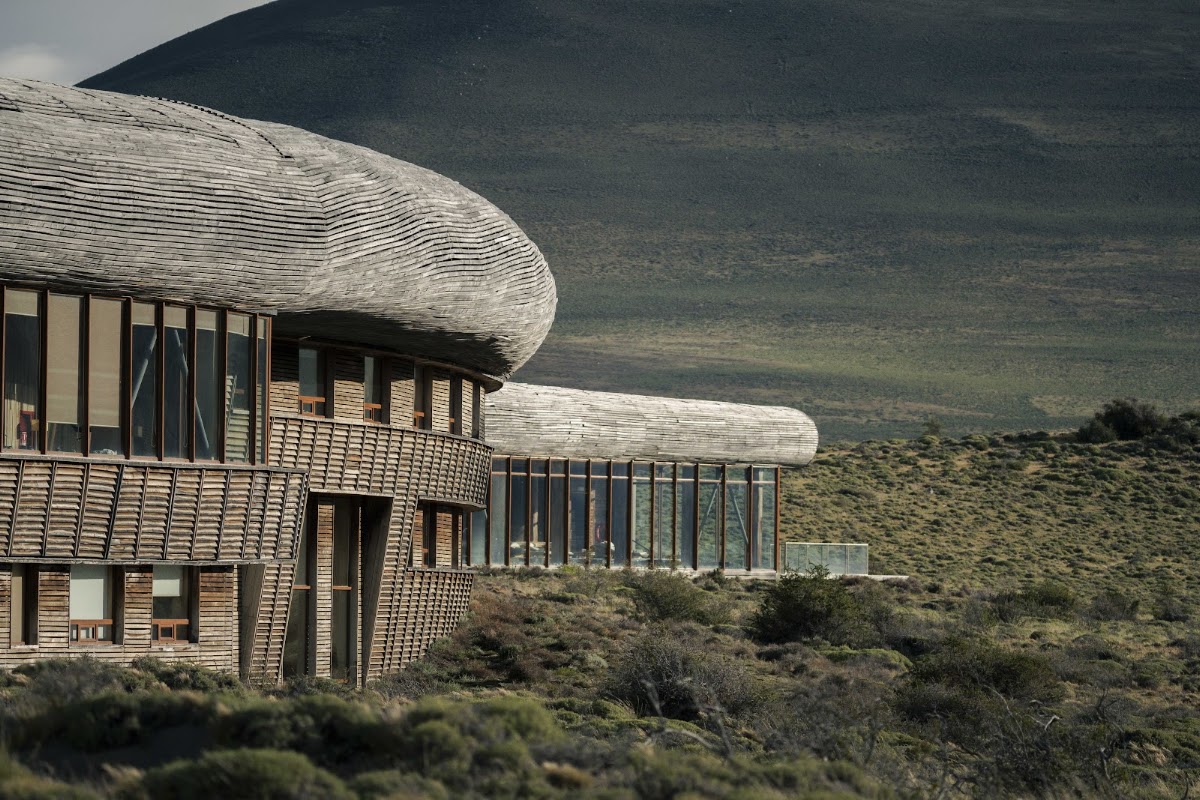Modern wooden lodge with curved architecture set against a volcanic mountain and arid Patagonian landscape at Tierra Patagonia.