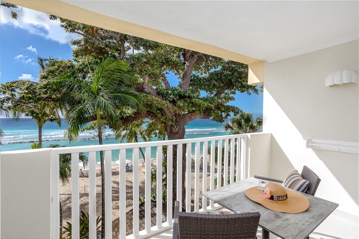View from a room balcony overlooking the pool area with white umbrellas, palm trees, and multi-story white resort buildings at Sugar Bay Barbados.