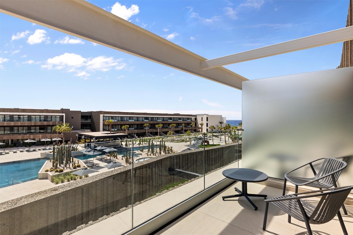 Modern oceanfront resort terrace with palm trees, lounge chairs, and bar area overlooking the Caribbean Sea at Secrets Baby Beach Aruba.