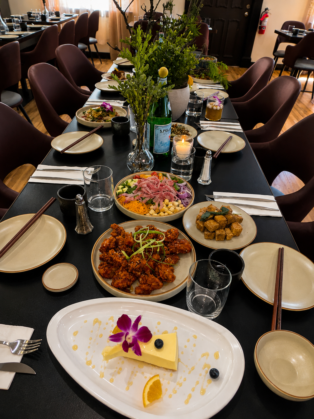 A long black dining table set with various Asian dishes, drinks, and a dessert.