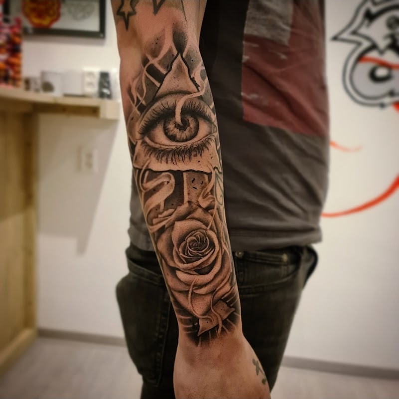Zwart-wit tattoo van een alziend oog in een driehoek en een roos op de onderarm.