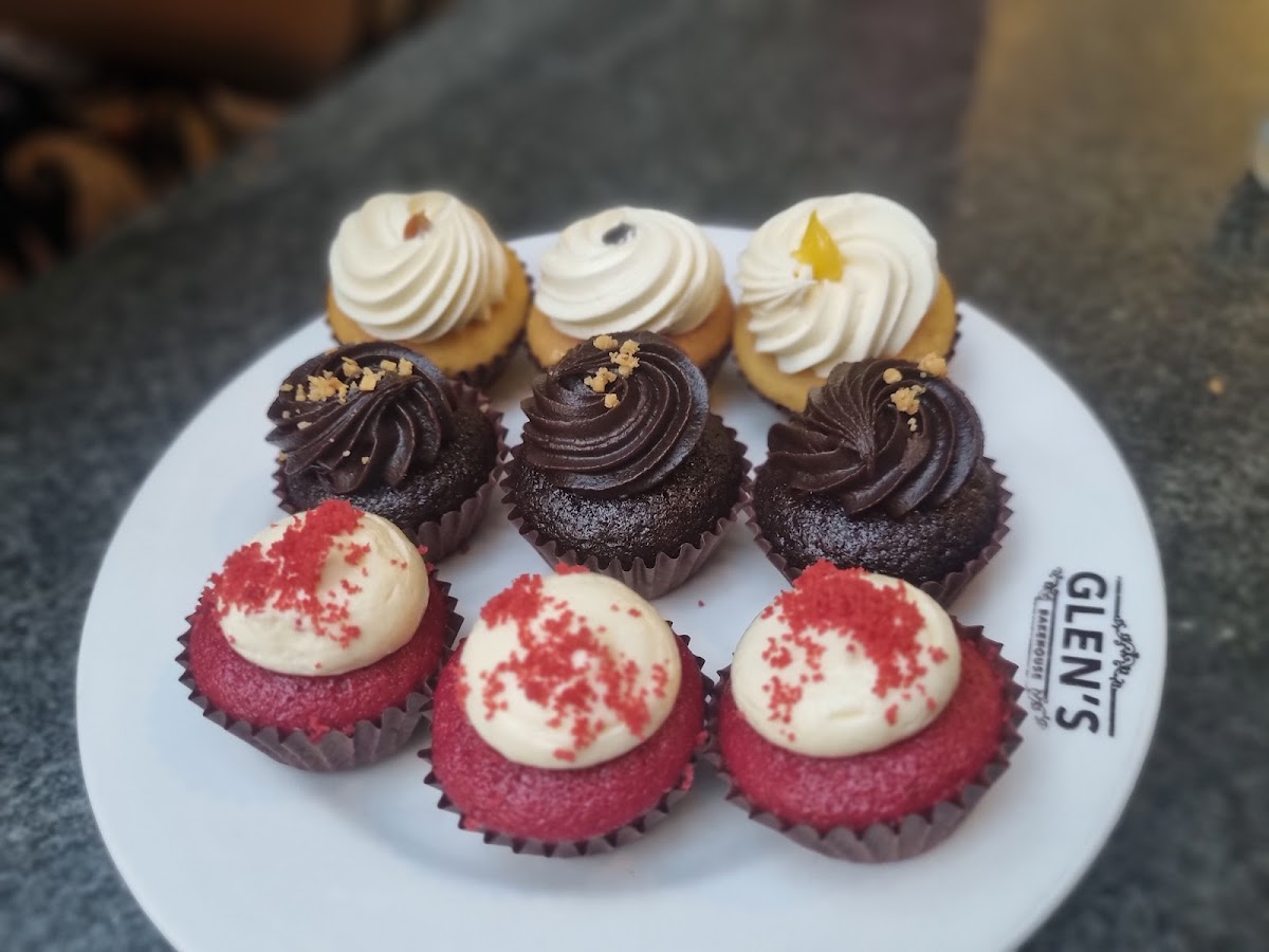 A delectable array of Glen's Bakehouse's signature cupcakes, showcasing flavors with rich chocolate, zingy lemon, and classic red velvet on an elegantly branded plate.
