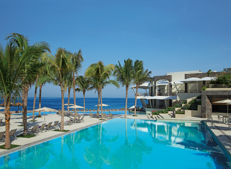 Turquoise pool with palm trees and loungers overlooking the ocean at Secrets Vallarta Bay.