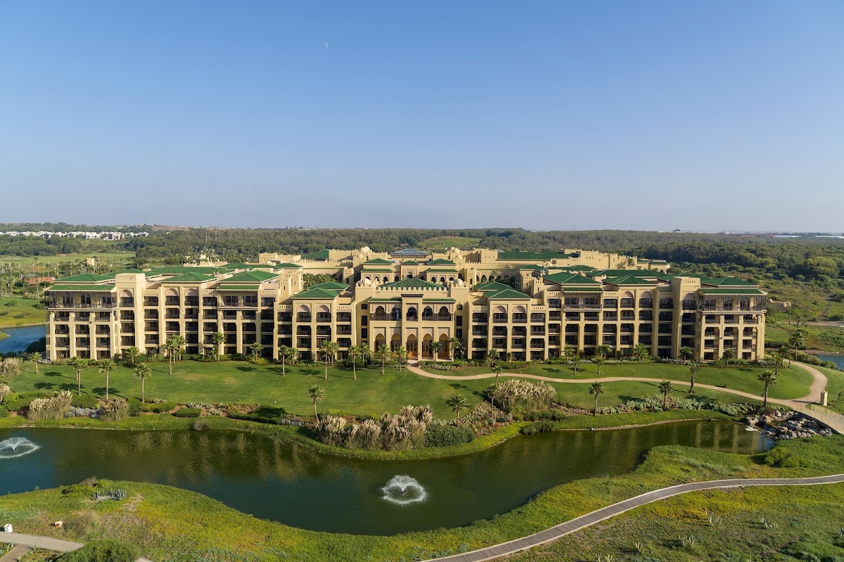 Clay tennis courts surrounded by palms and manicured grounds at Mazagan Beach & Golf Resort, with the ocean and beach visible beyond.