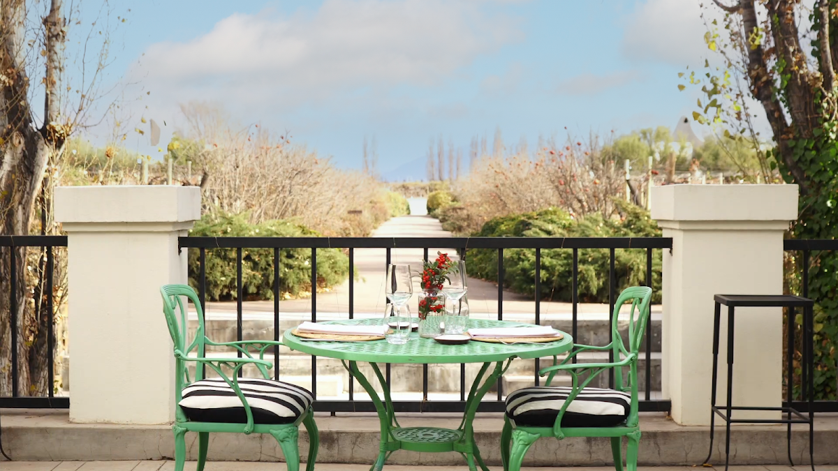 Green bistro chairs at a round table set for dining on a terrace at Awasi Mendoza, with desert hills visible beyond the railing.