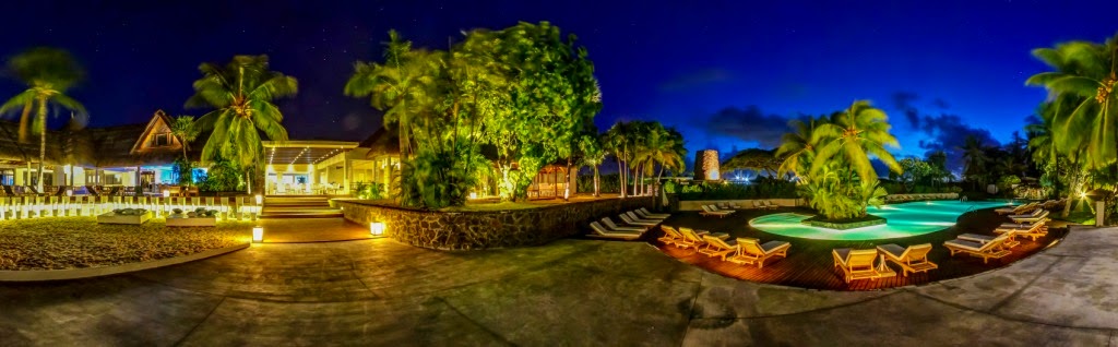 Solana Beach Mauritius resort illuminated at dusk with lit buildings, palm trees, and lounge chairs surrounding a turquoise pool.