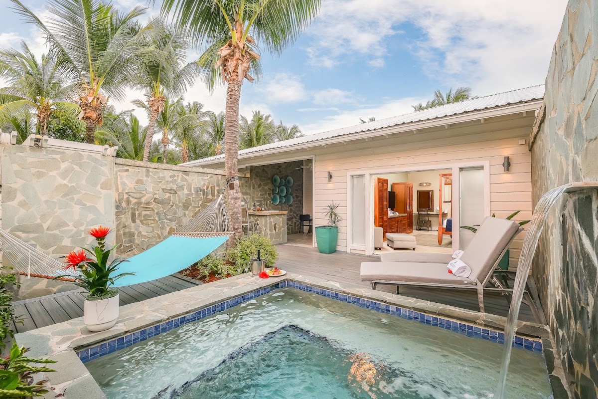 Private villa courtyard at Serenity at Coconut Bay with turquoise plunge pool, loungers, and pink cottage beyond palm trees.
