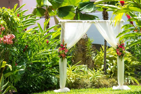 White draped wedding arch surrounded by pink and red tropical flowers and lush green foliage at The House, Barbados.