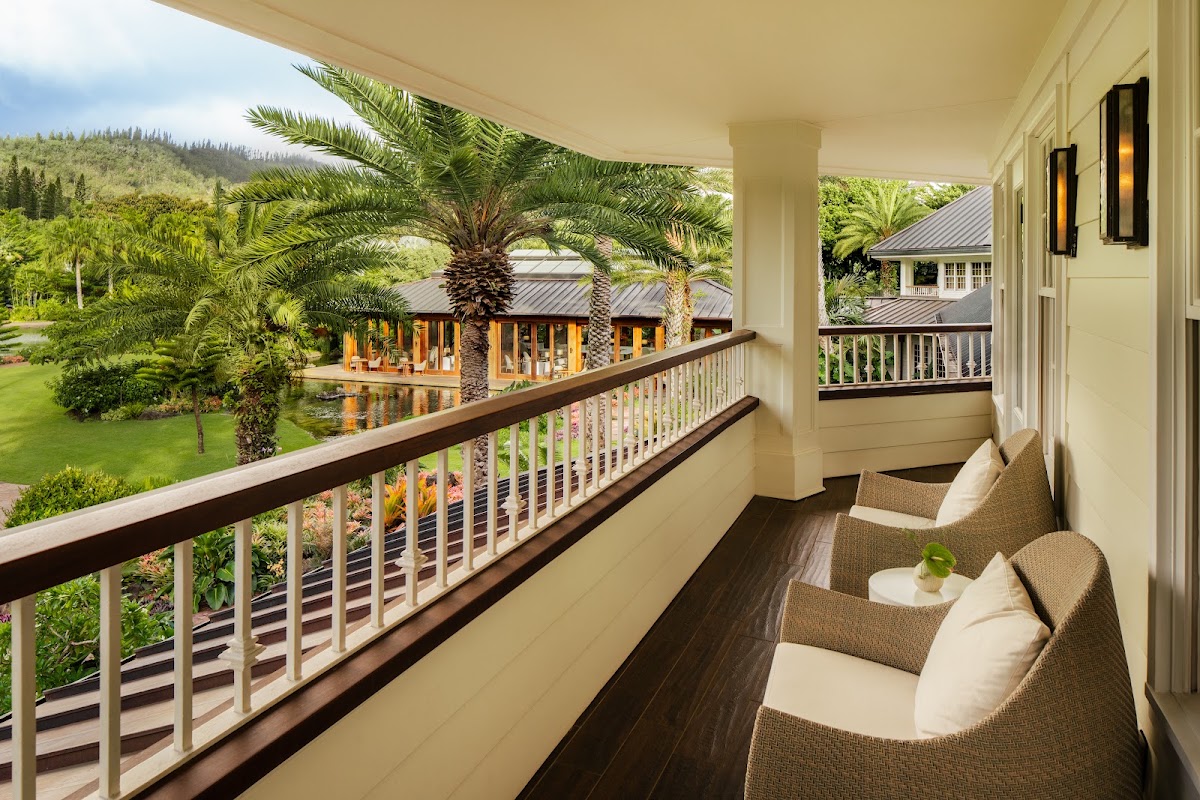 Modern wooden pavilion with floor-to-ceiling windows overlooks a calm lagoon surrounded by palm trees at dusk.