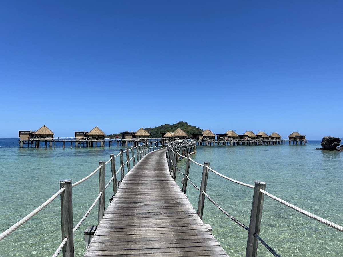 Wooden boardwalk stretches toward thatched bungalows built over turquoise lagoon water at Likuliku Lagoon Resort.