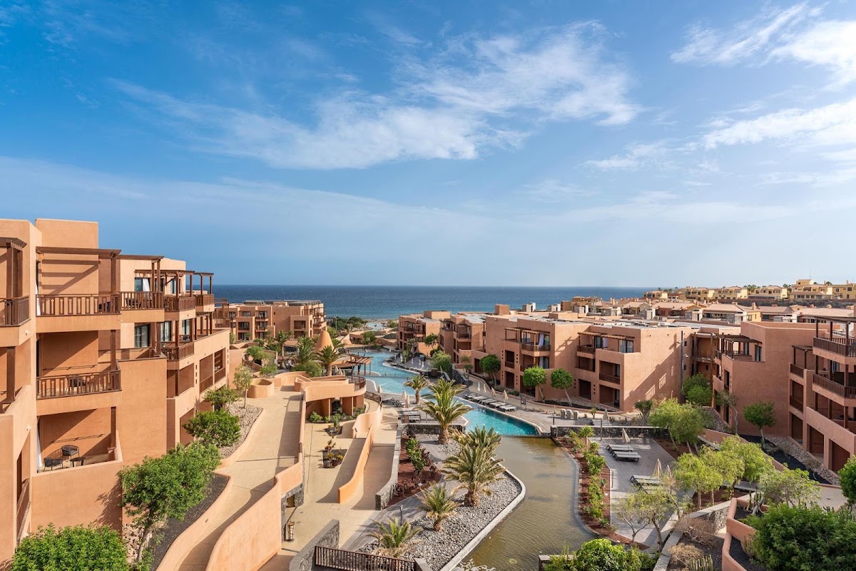 Terracotta resort buildings overlook pools, palm trees, and the ocean under blue sky at Barceló Tenerife.
