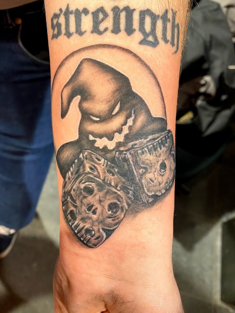 Zwart-wit tattoo van Oogie Boogie met schedel-dobbelstenen en 'strength' tekst.