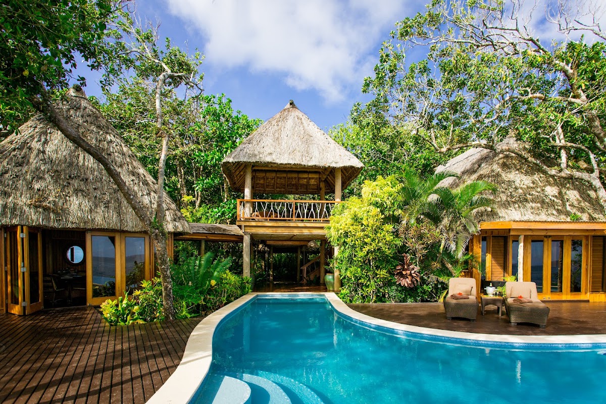 Thatched-roof bungalows with wooden decks surround a curved swimming pool at Namale Resort & Spa, surrounded by tropical vegetation.