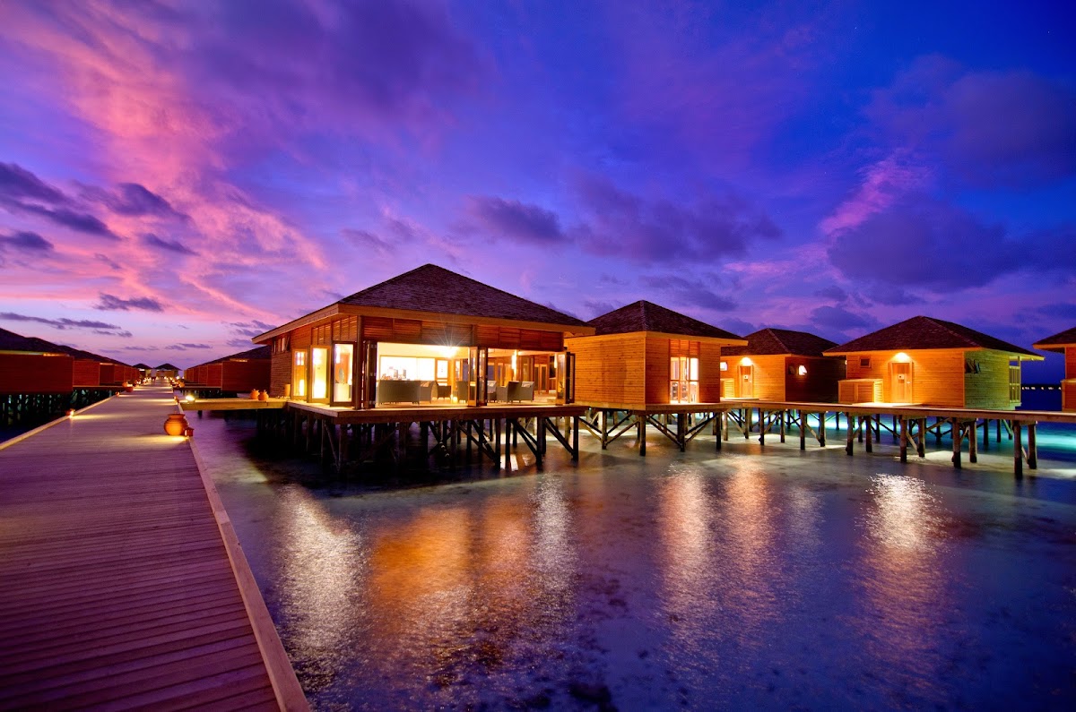 Aerial view of Vilamendhoo Island Resort & Spa's overwater bungalows arranged in symmetrical rows along a wooden jetty in turquoise lagoon waters.