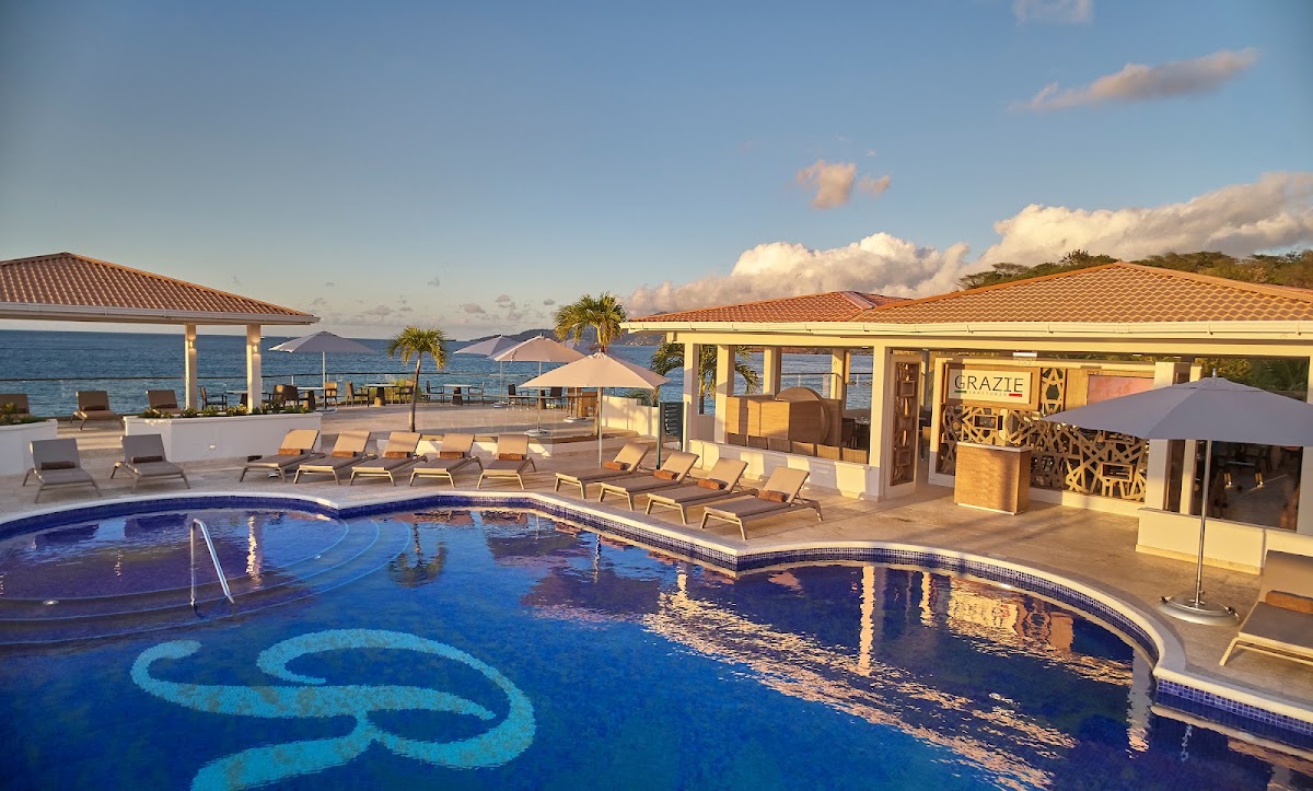 Royalton Grenada pool deck with lounge chairs, beachfront bar, and ocean view at sunset.