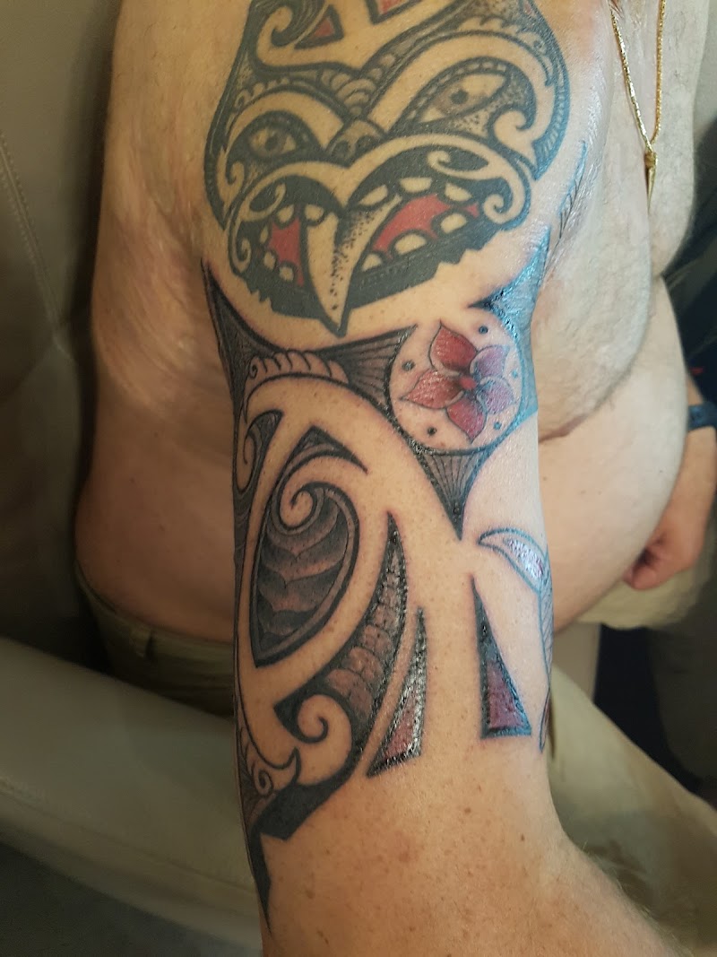 Tribal tattoo op bovenarm met rode accenten en een bloem.