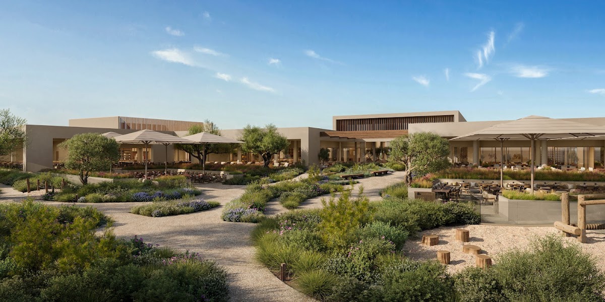 Resort courtyard with stone buildings, desert landscaping, umbrellas, and seating areas under pergolas.