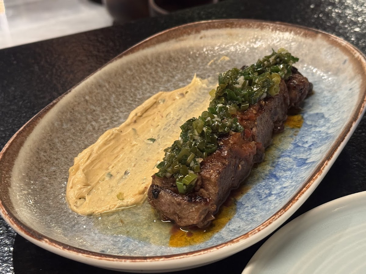 Comal's expertly grilled steak topped with fresh herbs and a side of creamy spread, showcasing their artisanal flair.