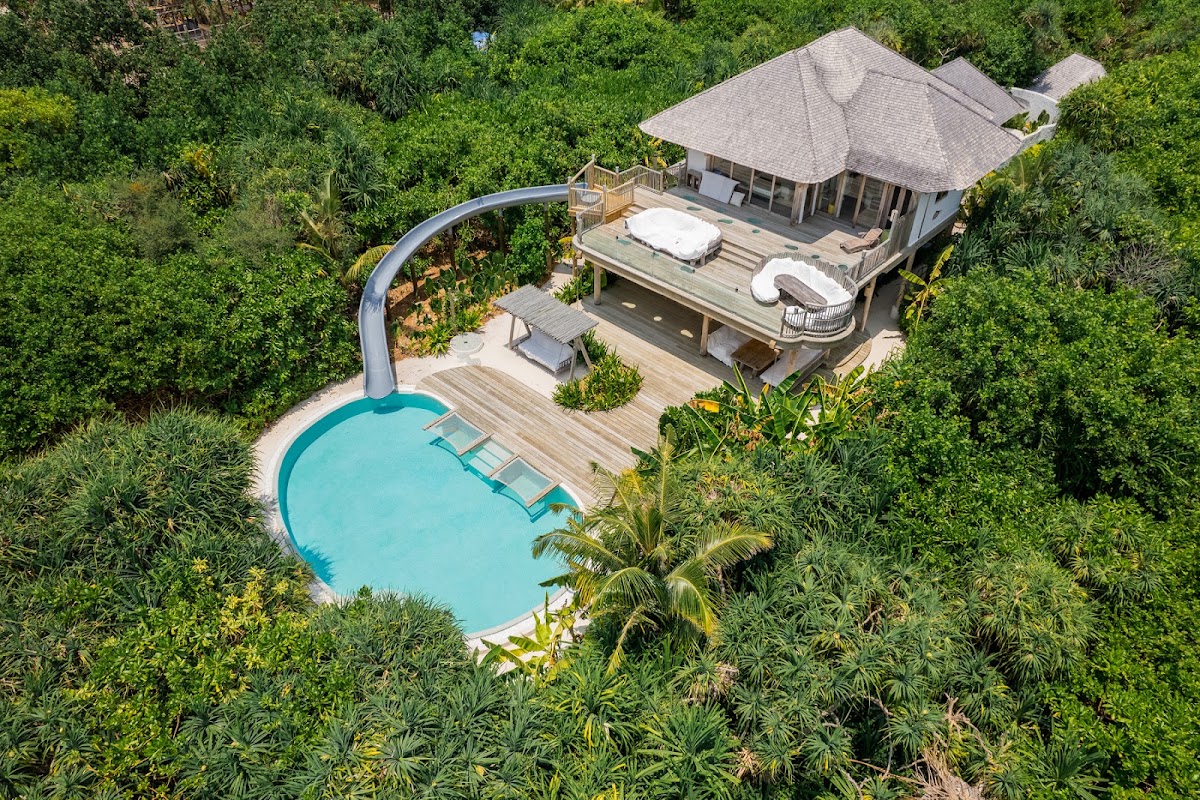Aerial view of a villa with turquoise pool and waterslide nestled in dense tropical vegetation at Soneva Jani.