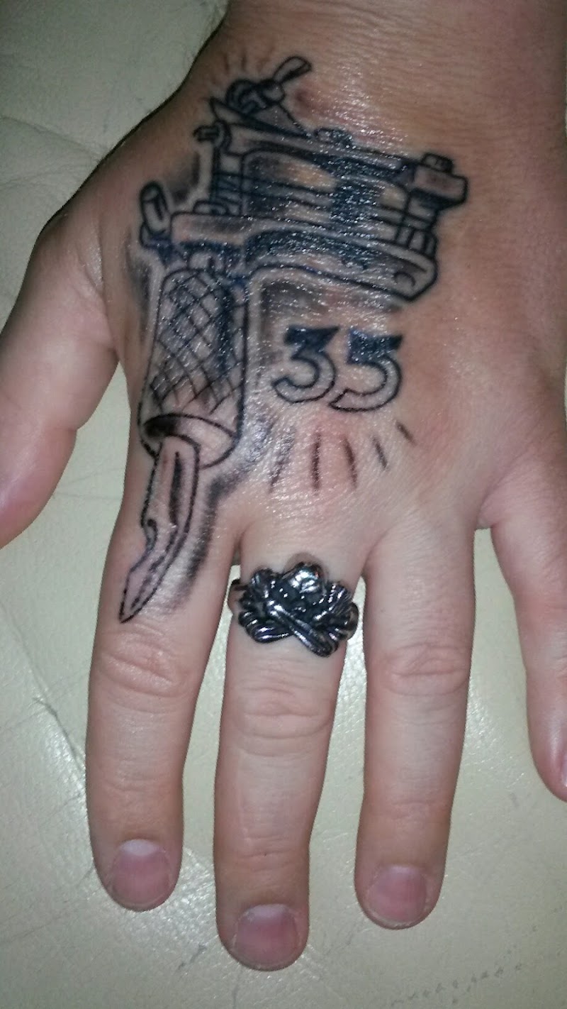 Blackwork tattoo van een tattoo-machine en het getal 35 op een hand.